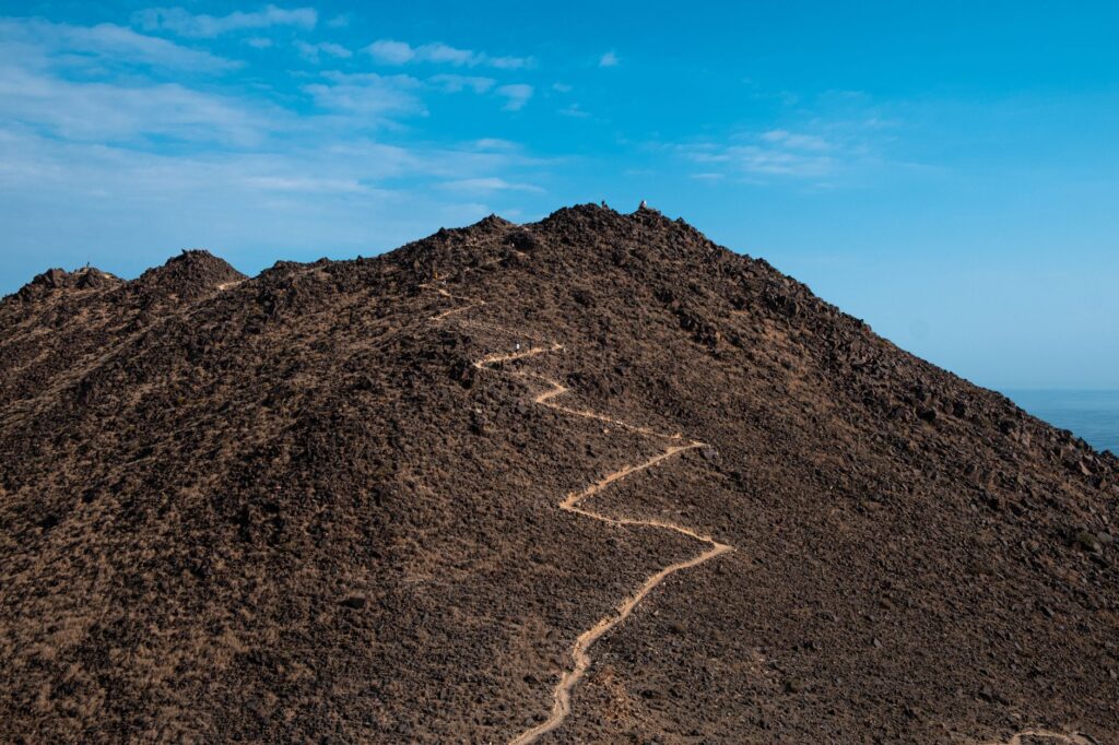 A winding trail on a rocky mountain summit under a vibrant blue sky, ideal for adventure seekers.