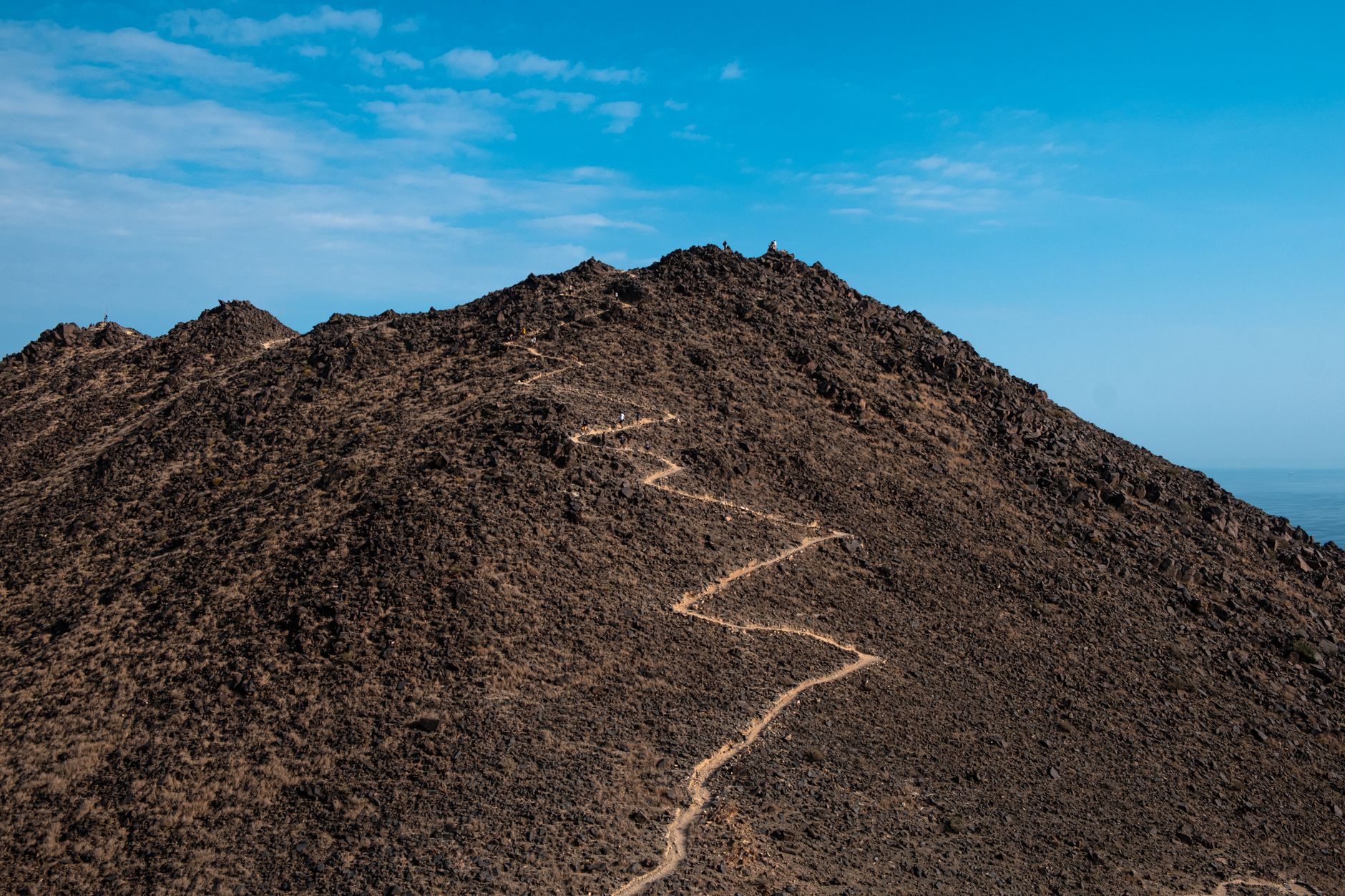 A winding trail on a rocky mountain summit under a vibrant blue sky, ideal for adventure seekers.
