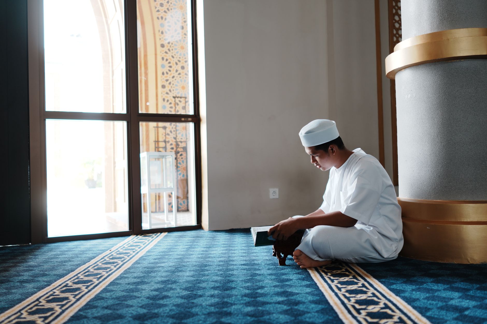 A man in white clothing kneeling in prayer inside a mosque, Indonesia.